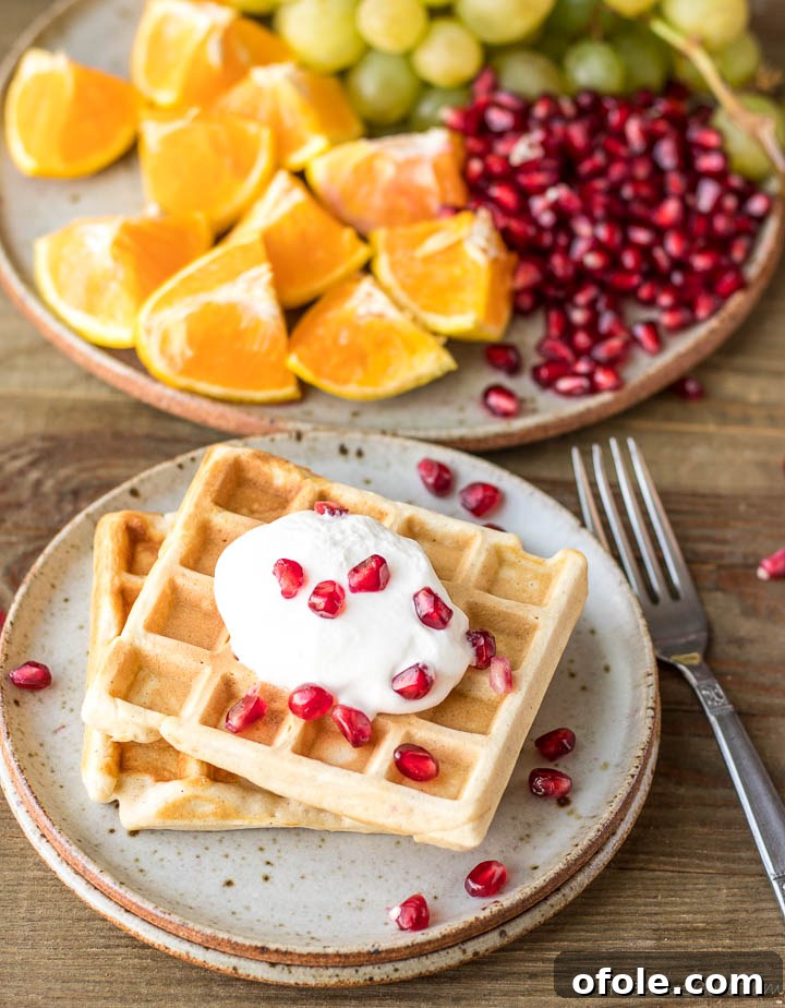 Kitchen-Crafted Waffles 3 Two fluffy homemade waffles topped with whipped cream and vibrant pomegranate seeds on a plate.