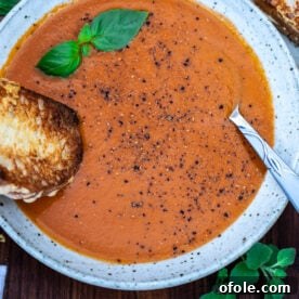 Roasted tomato and garlic soup in a bowl with a grilled cheese sandwich dipping into the soup, a classic comforting pairing.