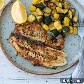 Lemon pepper tilapia on a plate with sautéed zucchini, a light and zesty fish dish.