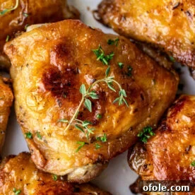 Close up on a golden brown chicken thigh, surrounded by other chicken thighs, showcasing the delicious crust.