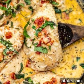 Wooden spoon under a piece of chicken breast in creamy sauce, showcasing the rich texture.
