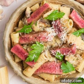 Creamy pasta in a bowl topped with juicy steak and mushrooms.