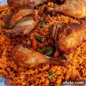 Jollof Rice on a serving platter with cooked chicken thighs and drumsticks on top, a festive meal.