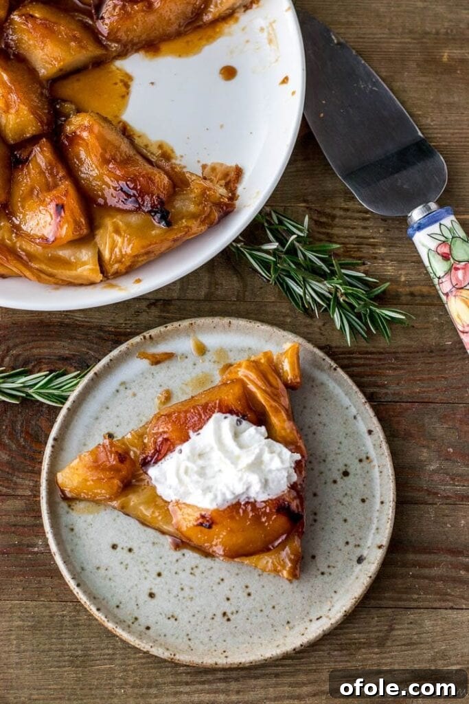 Slice of tarte tatin on a plate topped with cream, plate of large tarte tatin in the back