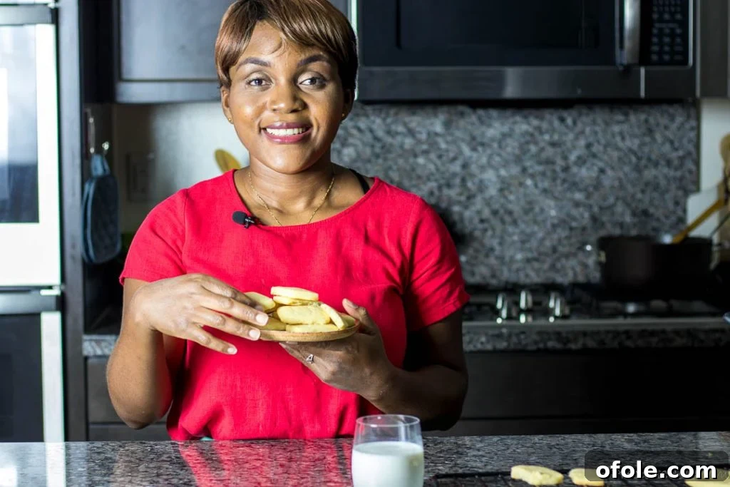 Fireside Chats 4 A smiling black woman stands confidently in a well-lit kitchen, holding a plate laden with freshly baked cookies, ready to share her culinary creation.