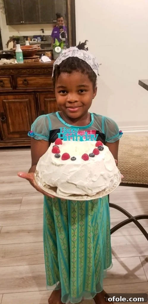Fireside Chats 6 A joyous young girl, dressed in an "Anna" inspired costume, proudly holds a beautiful white cake with colorful sprinkles and candles, adorned with the words "Happy Birthday."
