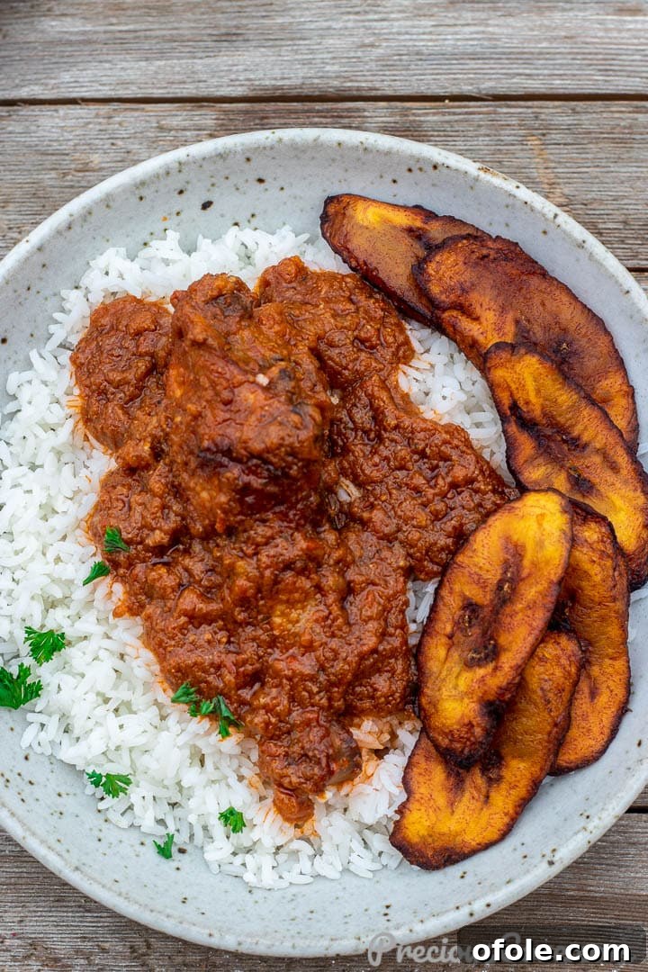 A generously filled bowl of African chicken stew served over fluffy white rice, adorned with fresh herbs.