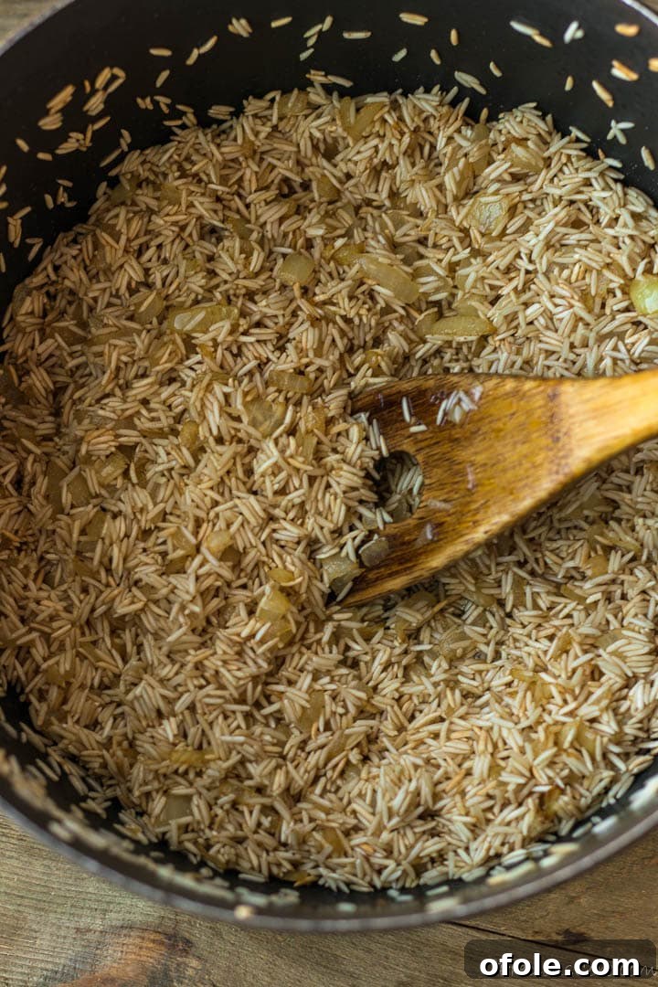 Raw Basmati rice toasting with sautéed onions and oil in a large pot.